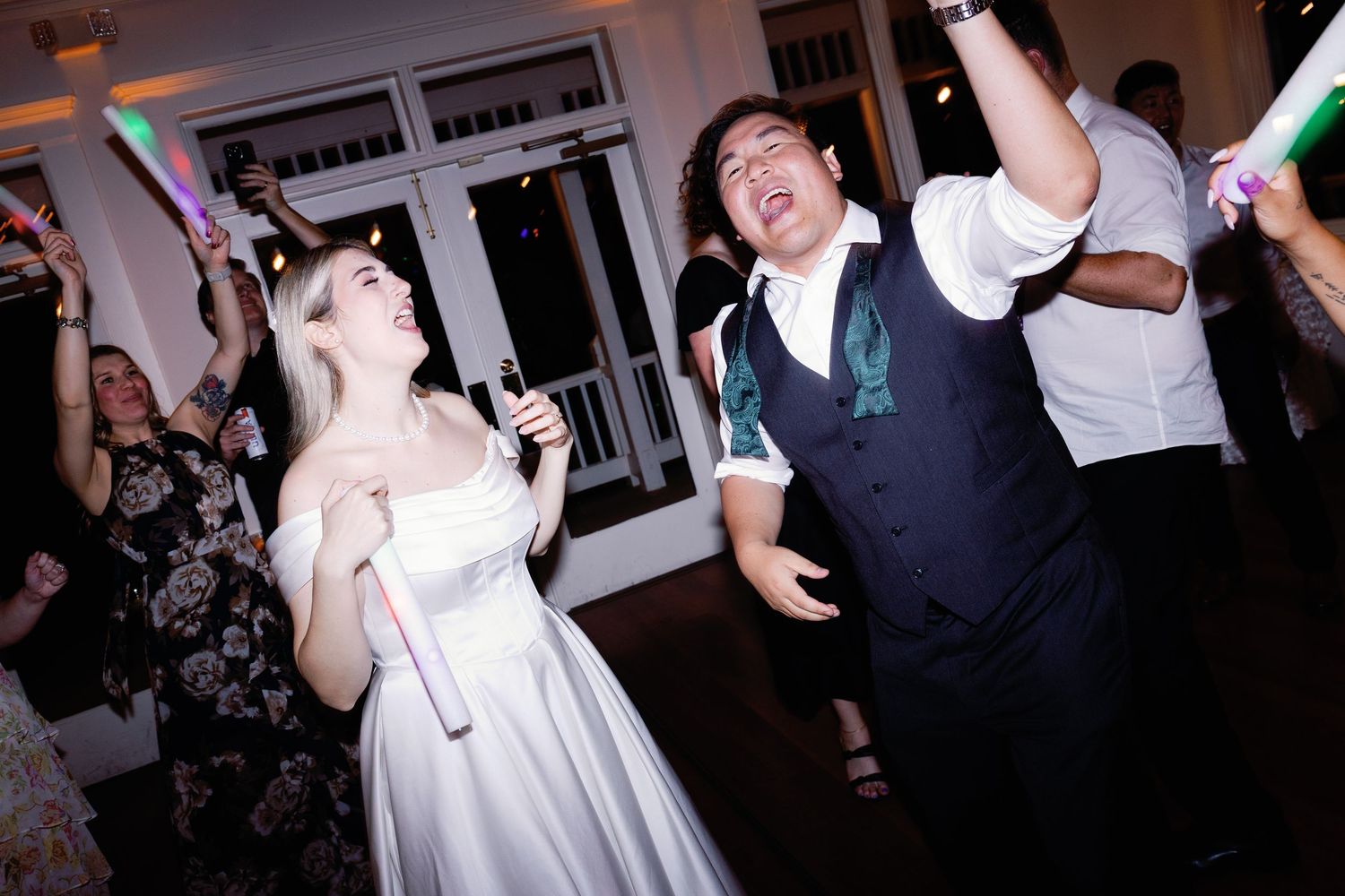 Wedding guests dance energetically while holding bright LED foam sticks at a reception.