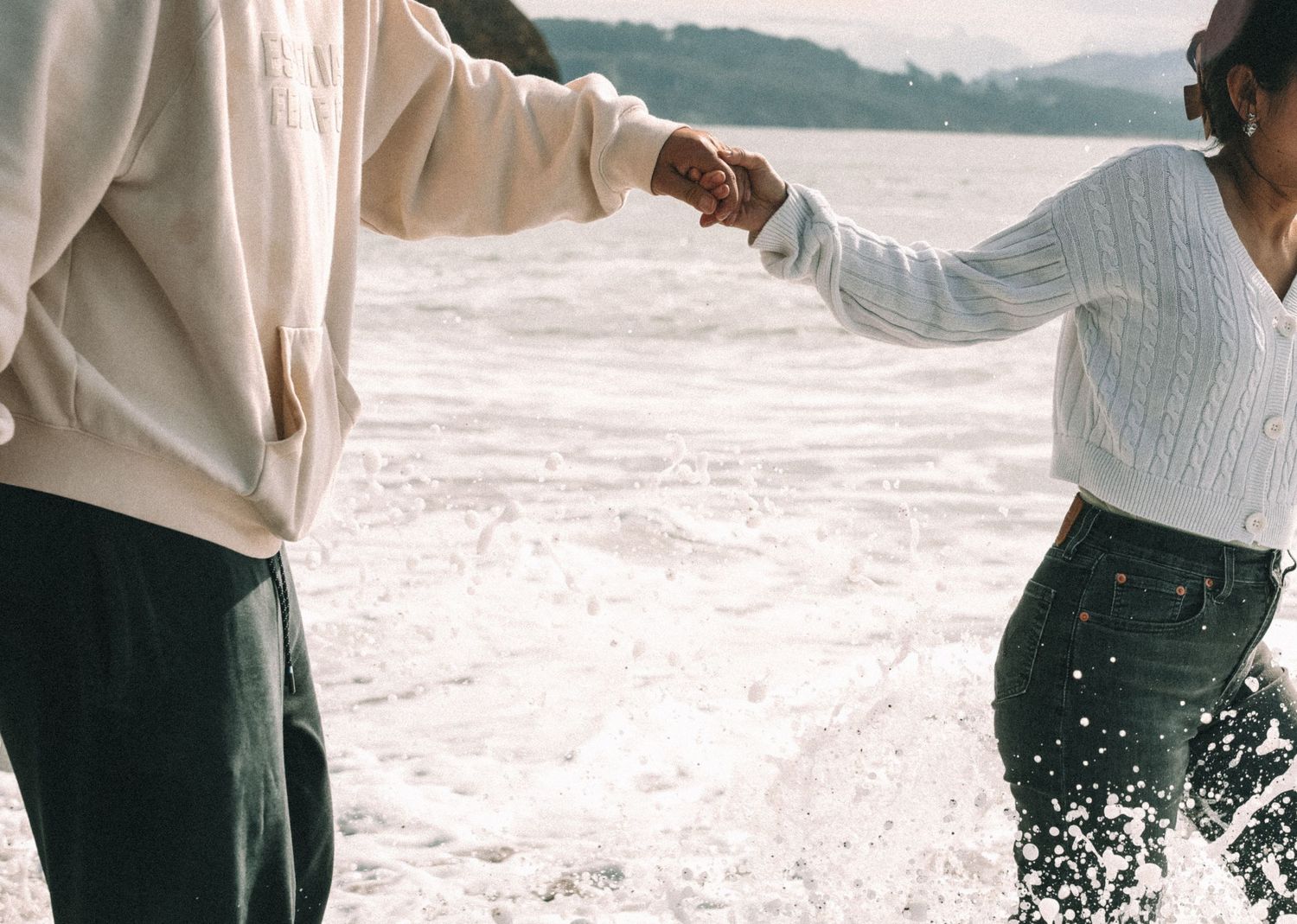 People splashing and playing in ocean waves on a beach with mountains in the background.