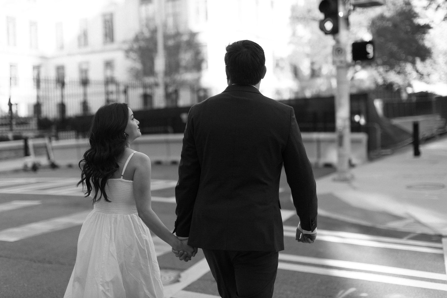 A couple shares an intimate silhouetted moment on an urban street with buildings in the background.