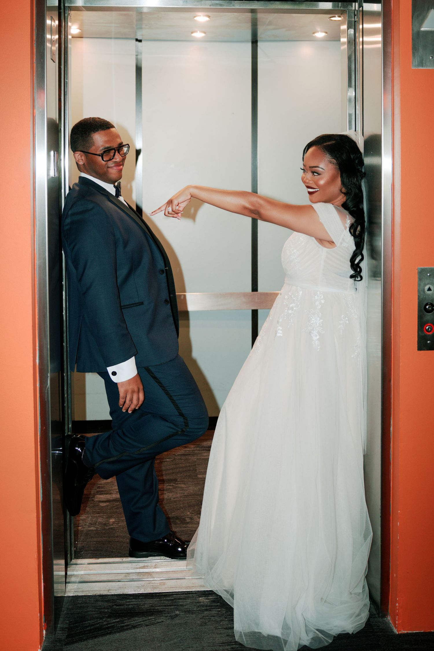 Playful wedding portrait of couple posing in modern elevator.