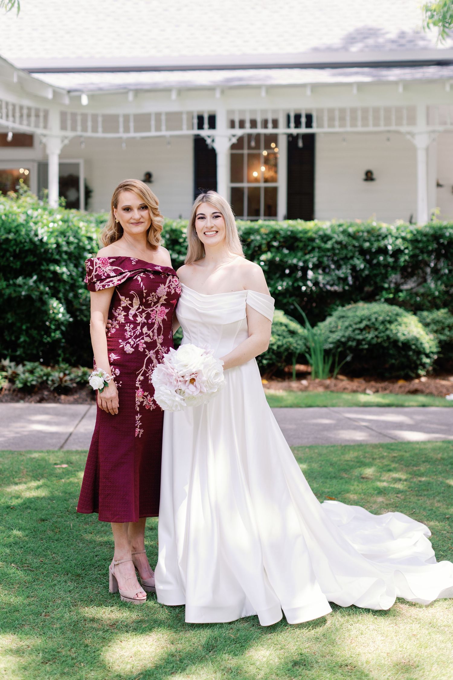 Wedding party wearing burgundy and white dresses posing in front of a white colonial-style building.