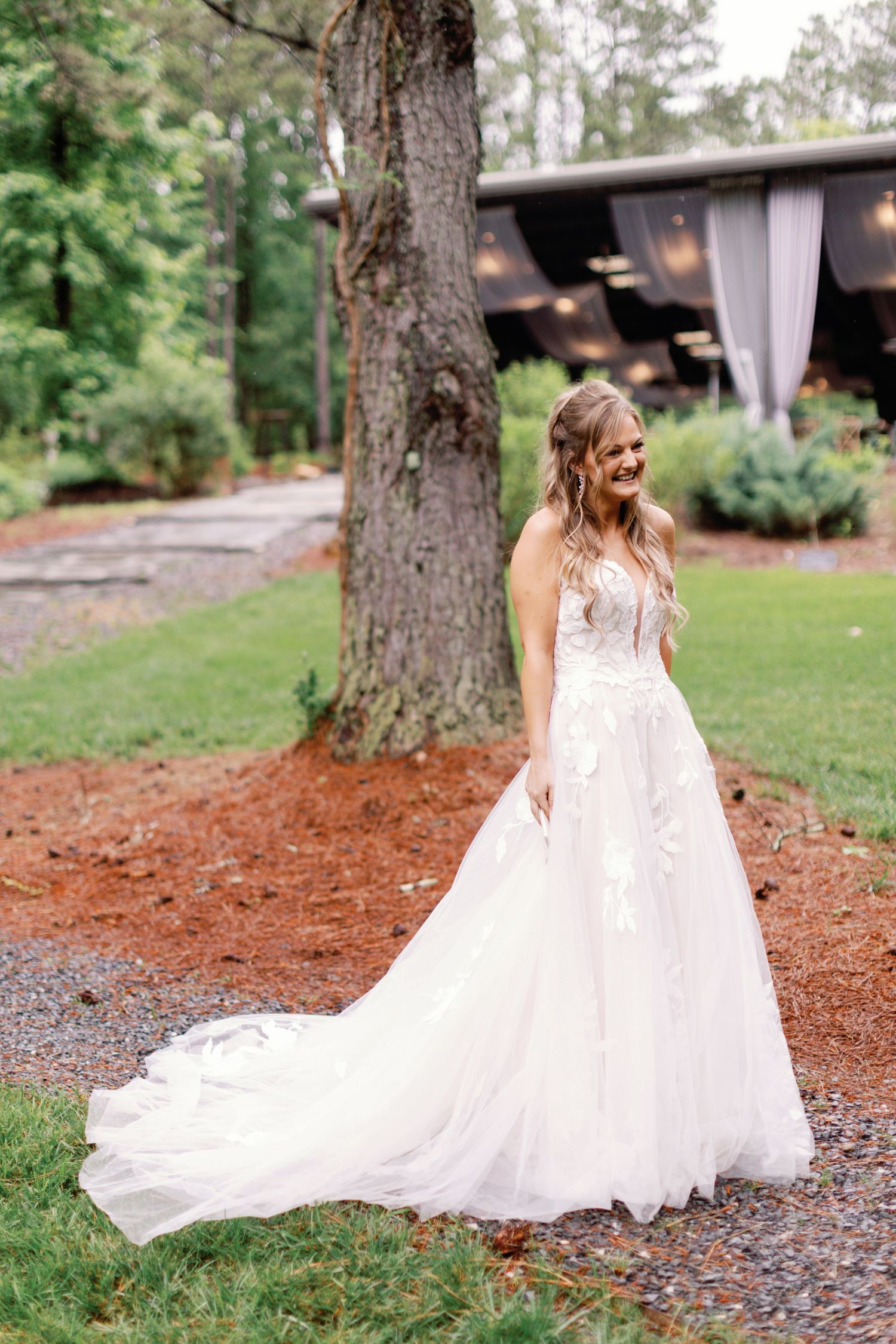 A flowing white wedding dress with lace details trails across a garden path.