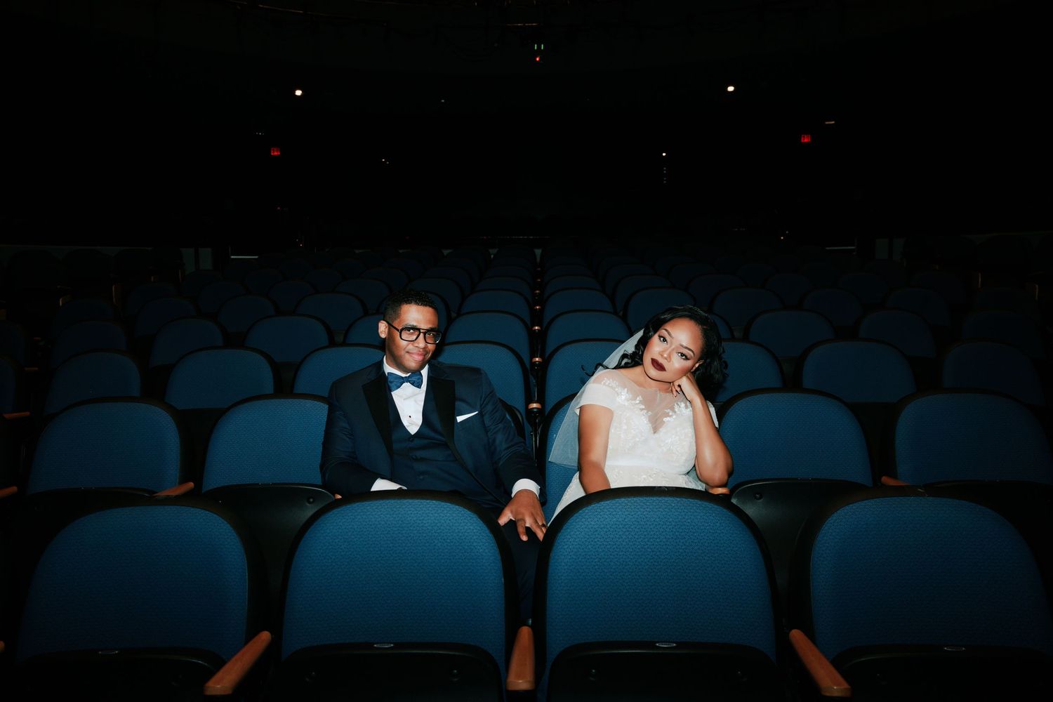 Wedding couple seated in dark blue theater seats during a creative photo session.
