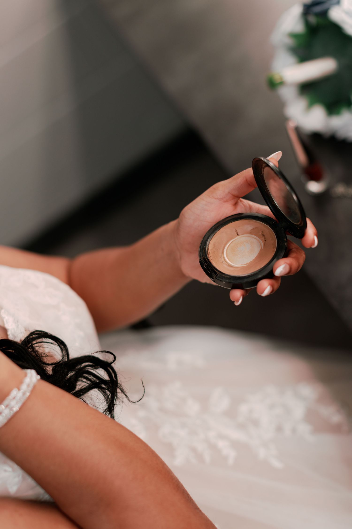 Hands applying makeup with a compact mirror in a soft, intimate beauty preparation setting.