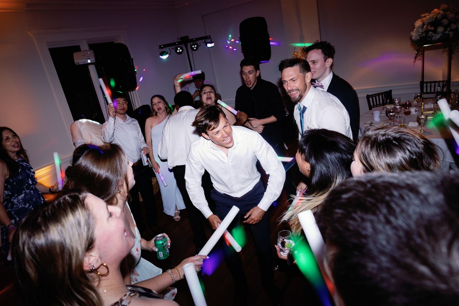 Partygoers wave illuminated LED sticks creating light trails in a dark reception hall.