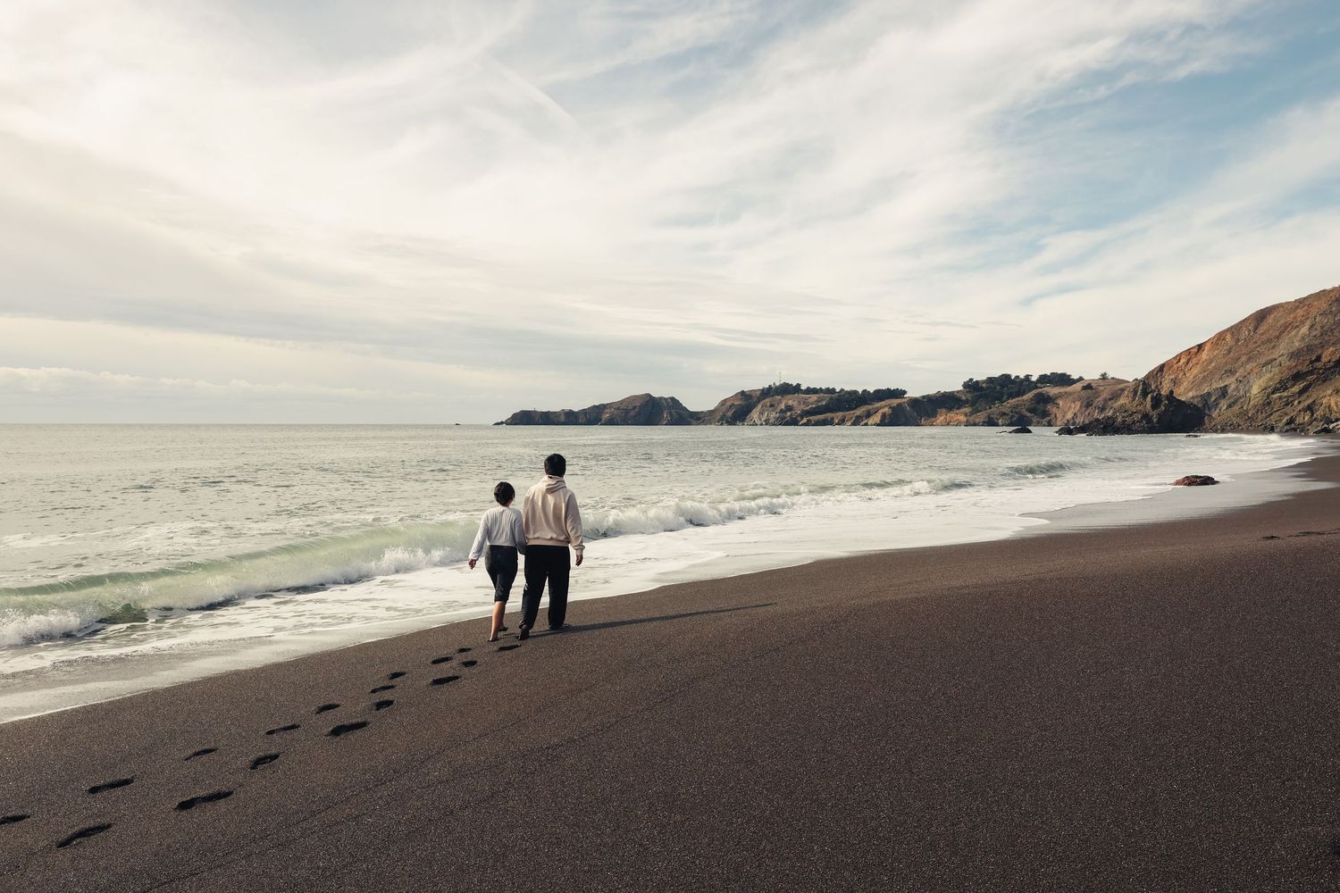 Scenic panorama of a rocky coastline with dark sand beach and rolling waves.