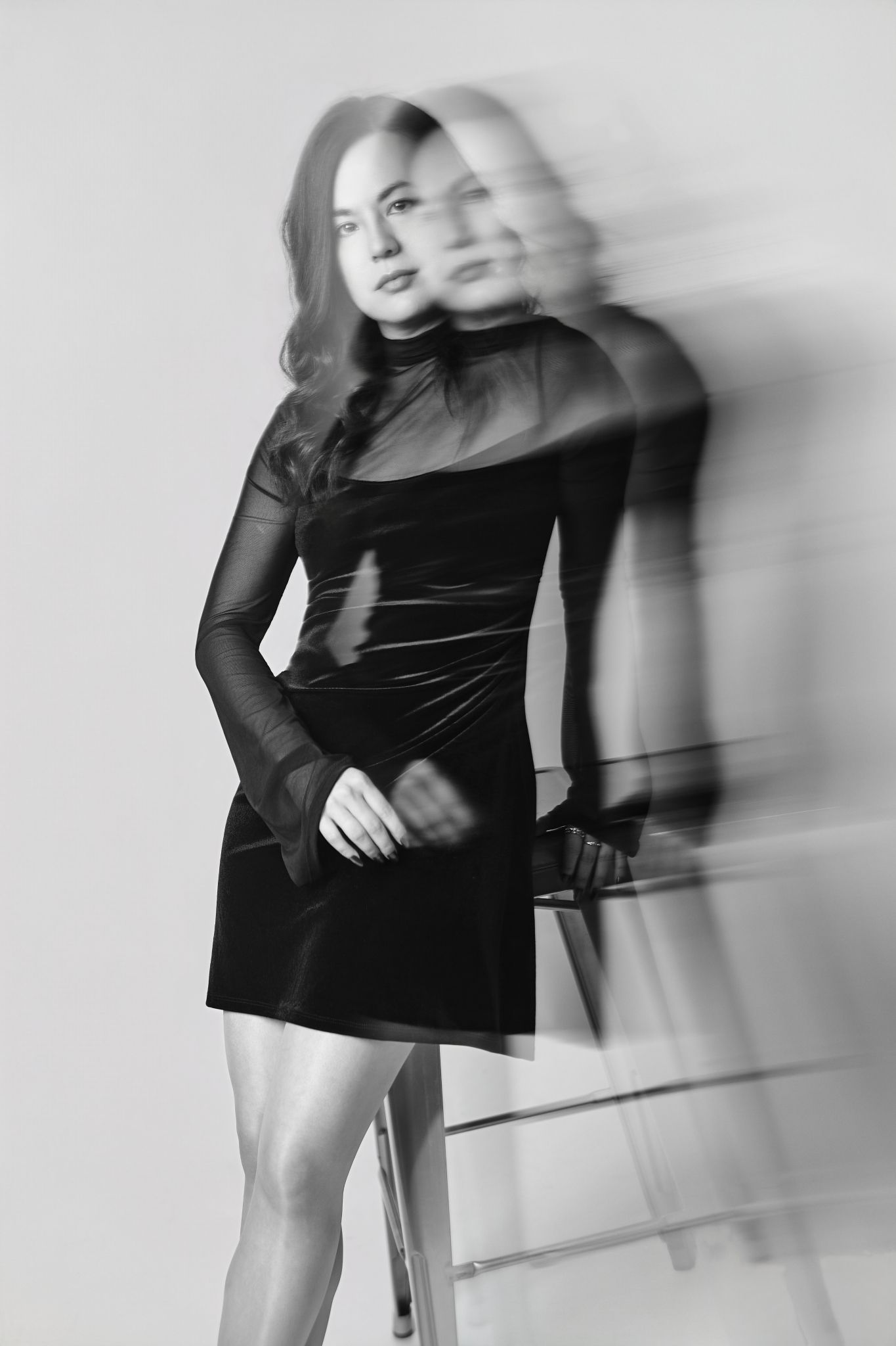 Black and white photo of a woman in a velvet mini dress with sheer sleeves, captured with a motion blur effect.