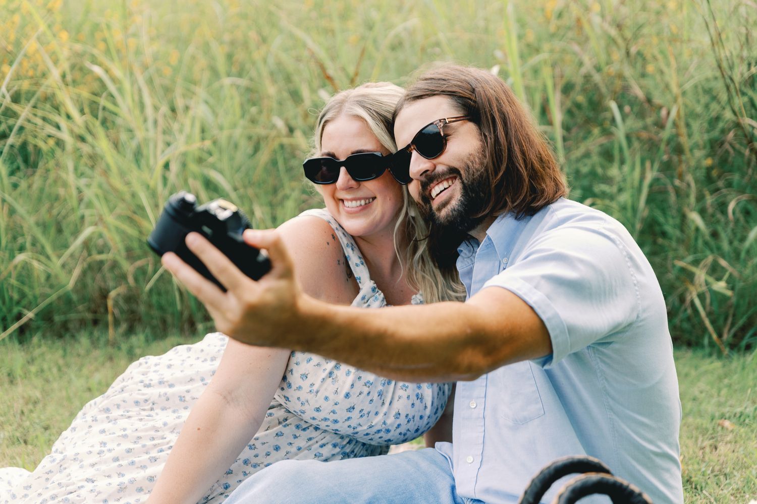 Playful couple laughing together in a sunny field of tall grass.