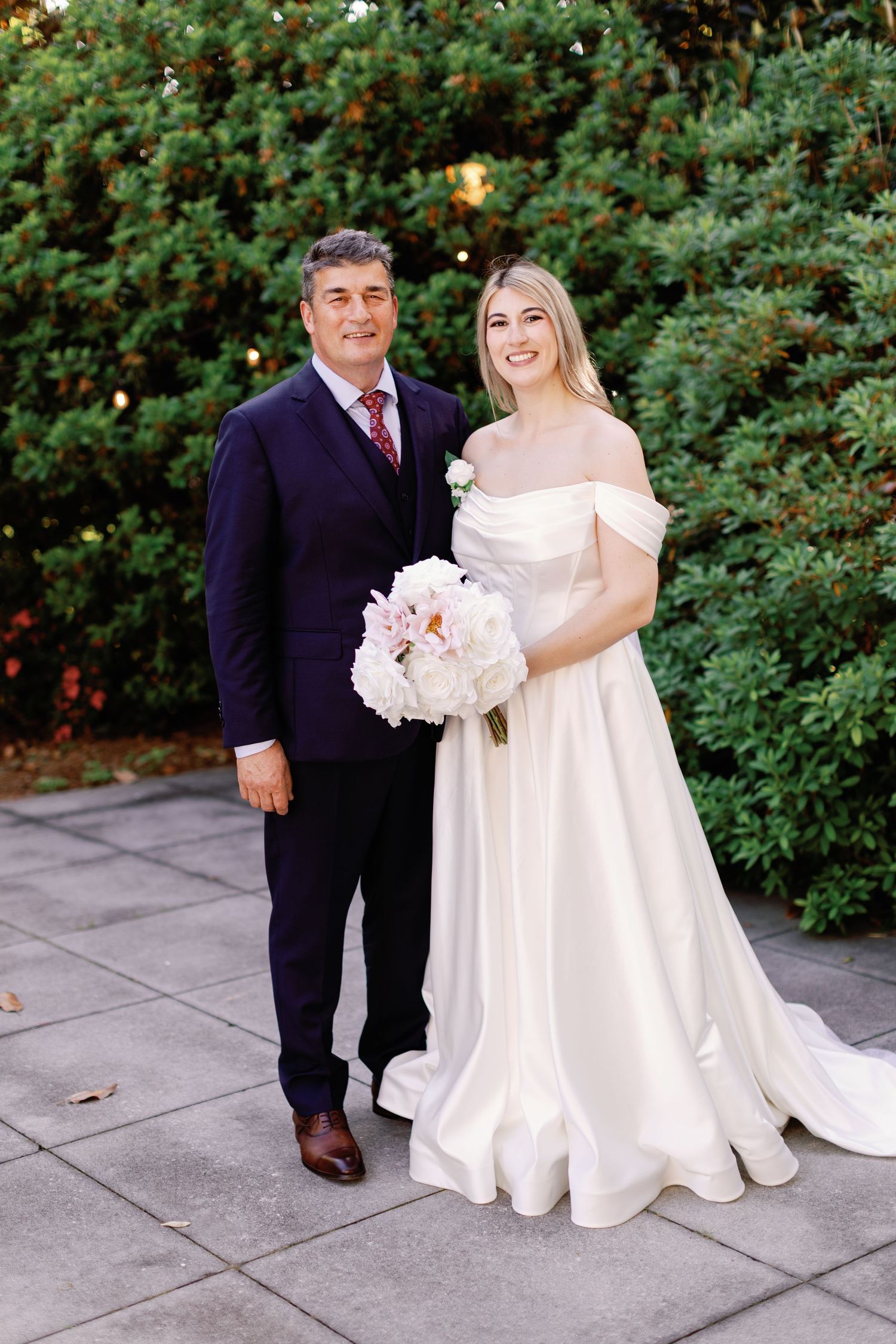Wedding portrait with white bouquet against lush green garden backdrop.