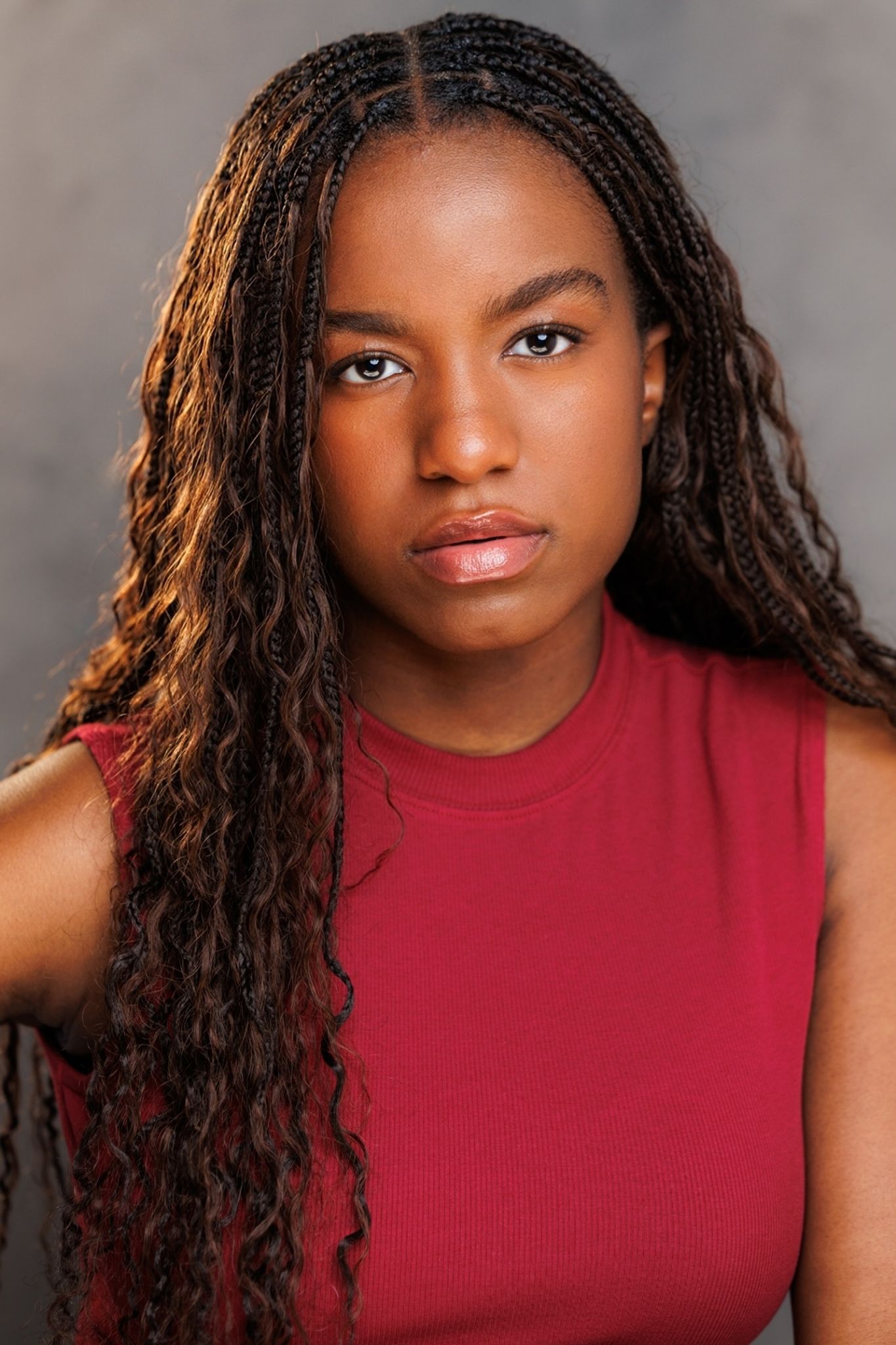 Young Black woman with long braided hair wearing a red sleeveless top, posing for a professional headshot.