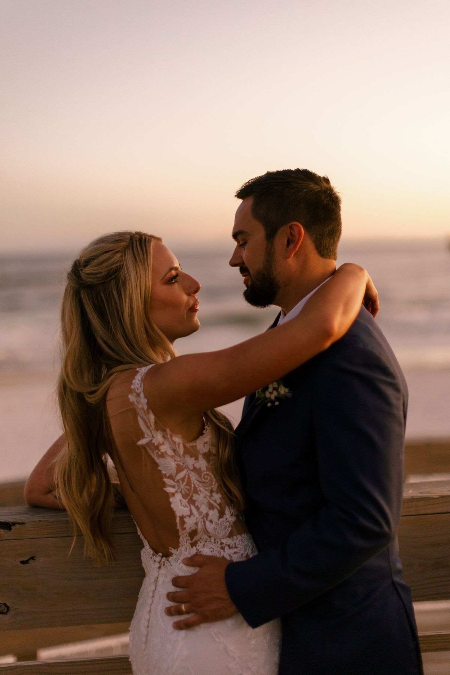 Couple shares intimate moments at sunset on wooden pier overlooking the ocean.