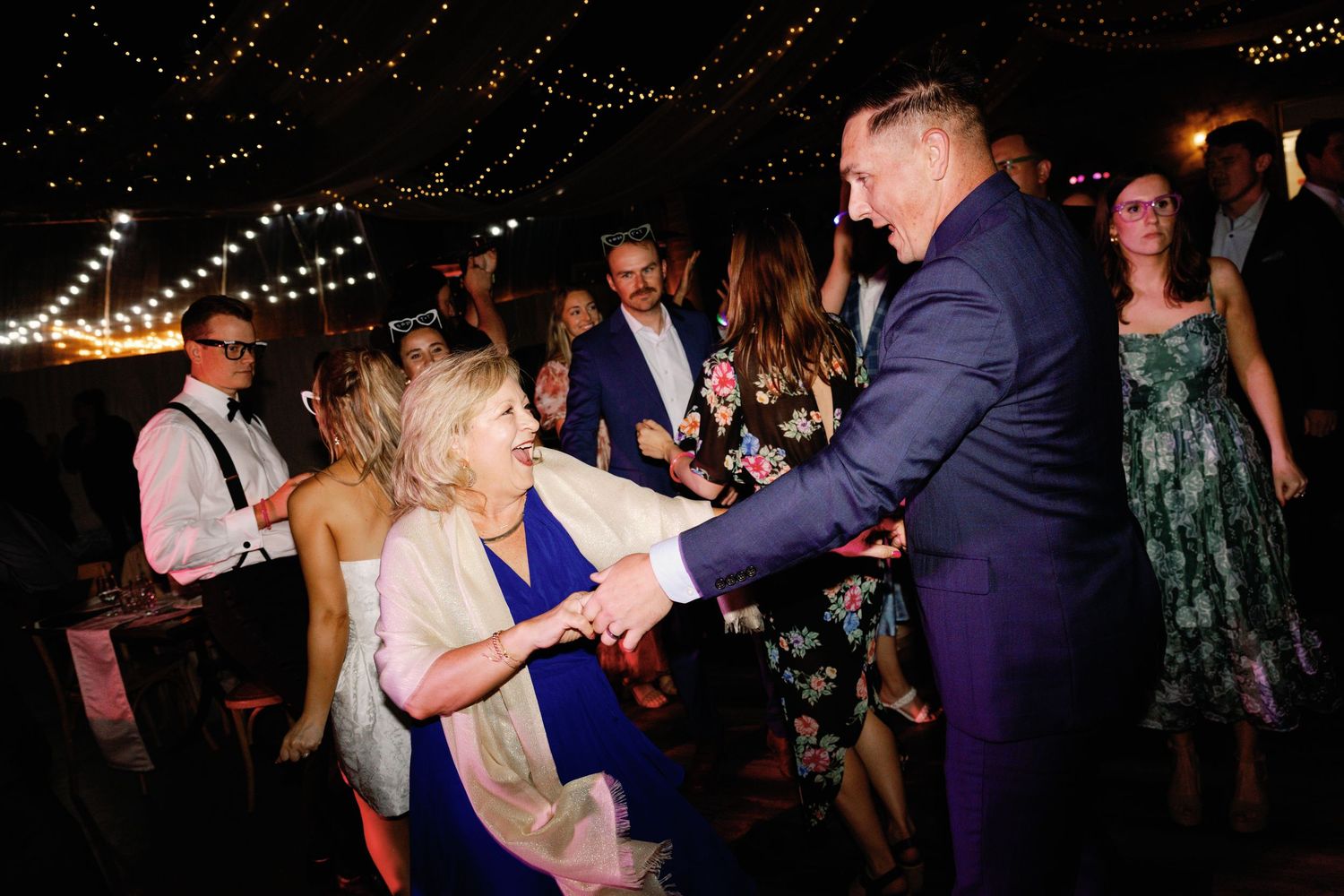 Party guests dancing and having fun under string lights at an indoor celebration.