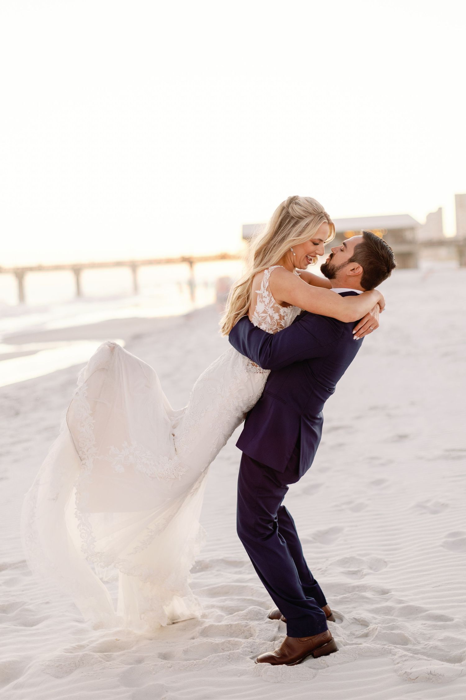 Joyful wedding couple embraces and spins on a scenic beach at golden hour.