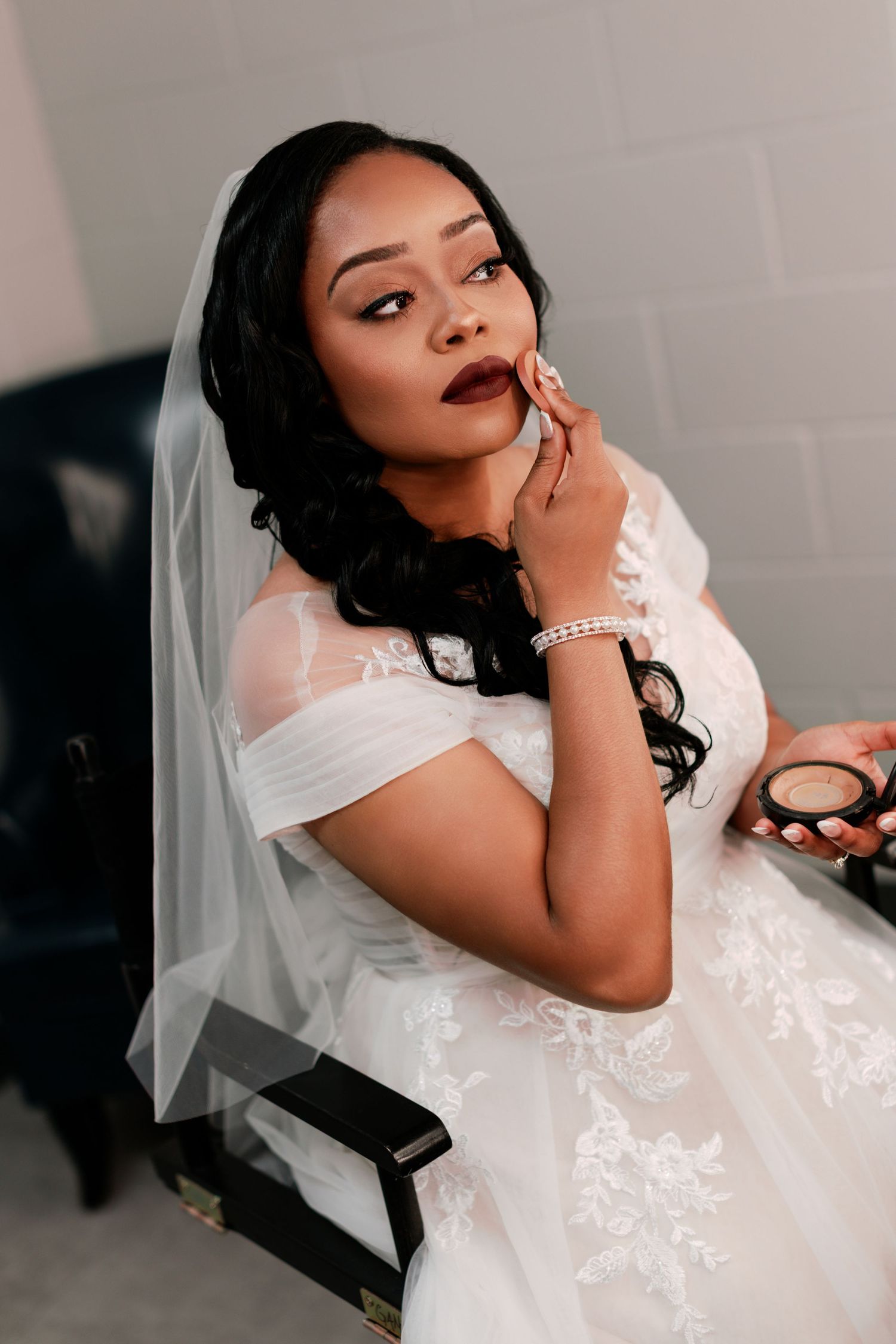 Bride in lace wedding dress thoughtfully posing beside vanity lights.