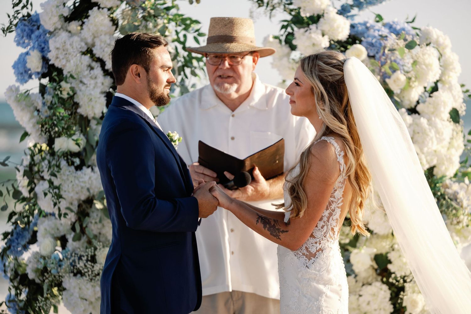 Wedding ceremony on beach with white floral arch and ocean view.