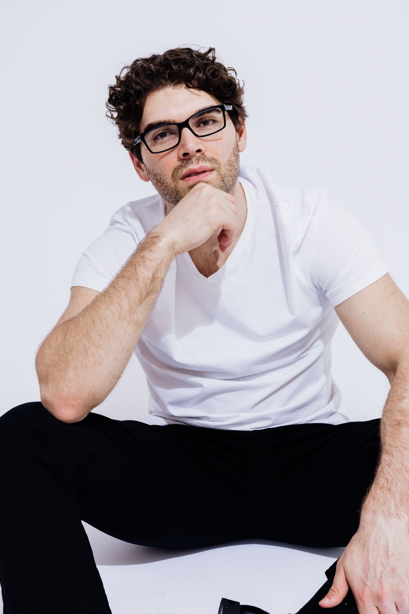Casual portrait series of a person in white t-shirt lounging against white backdrop.