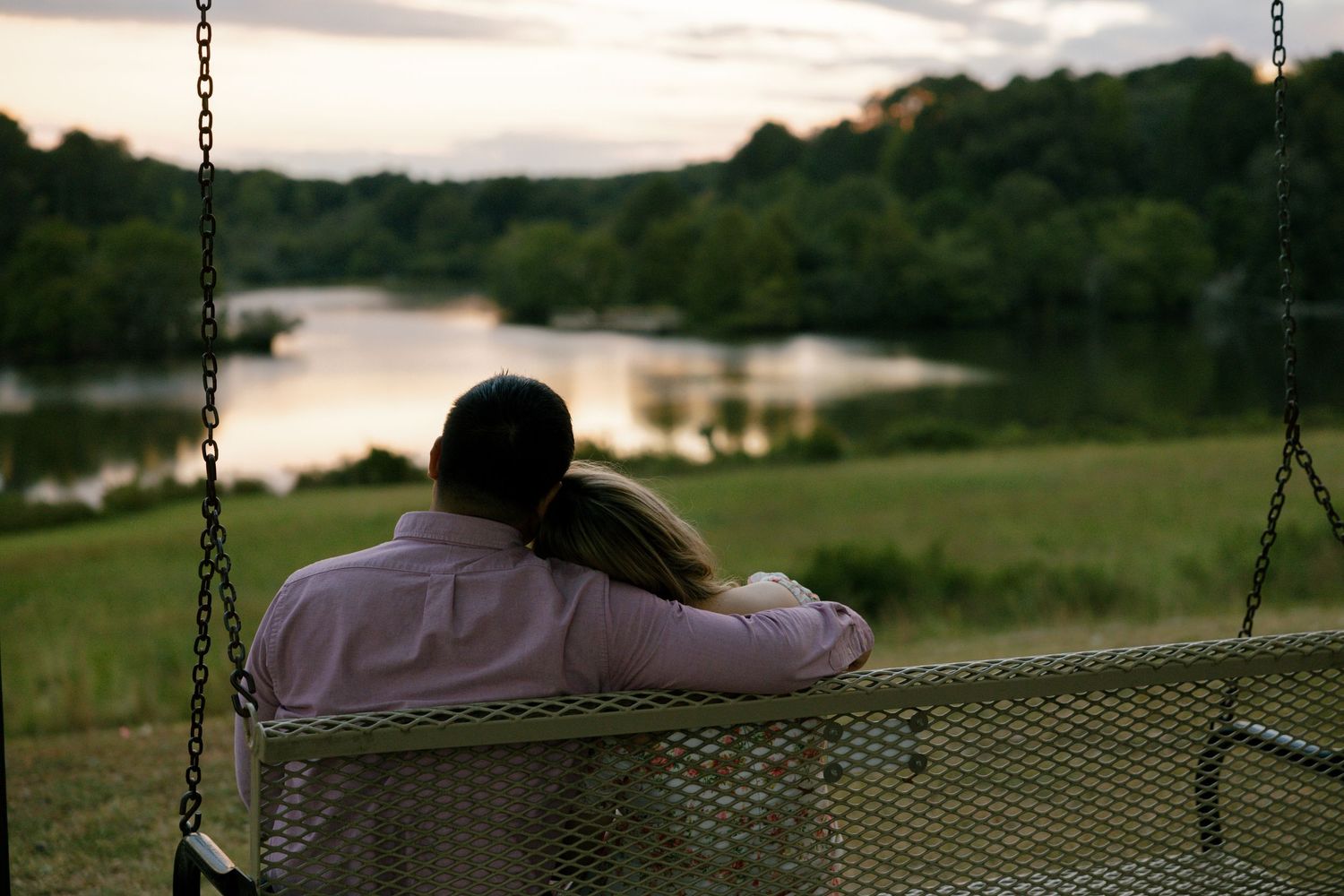Couple sitting together on a swing at sunset overlooking a peaceful lake.