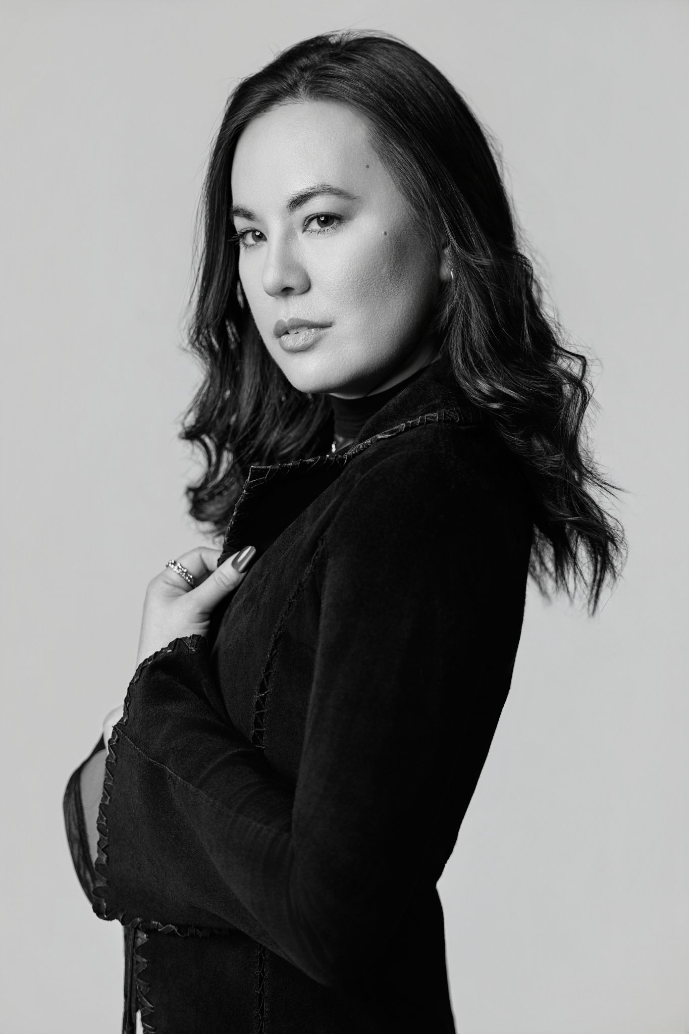 Black and white portrait of a young woman in a black turtleneck, posing with arms crossed against a light background.