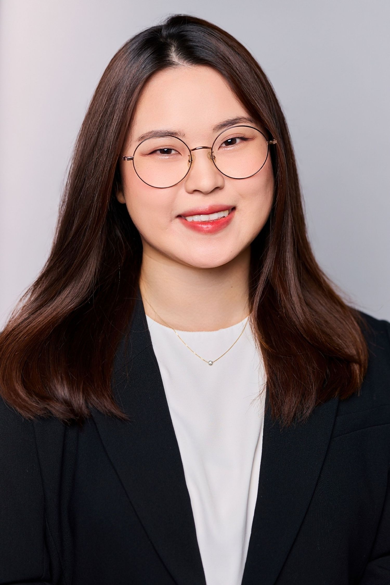 Young professional woman with glasses and dark hair smiling in a black blazer for a corporate headshot.