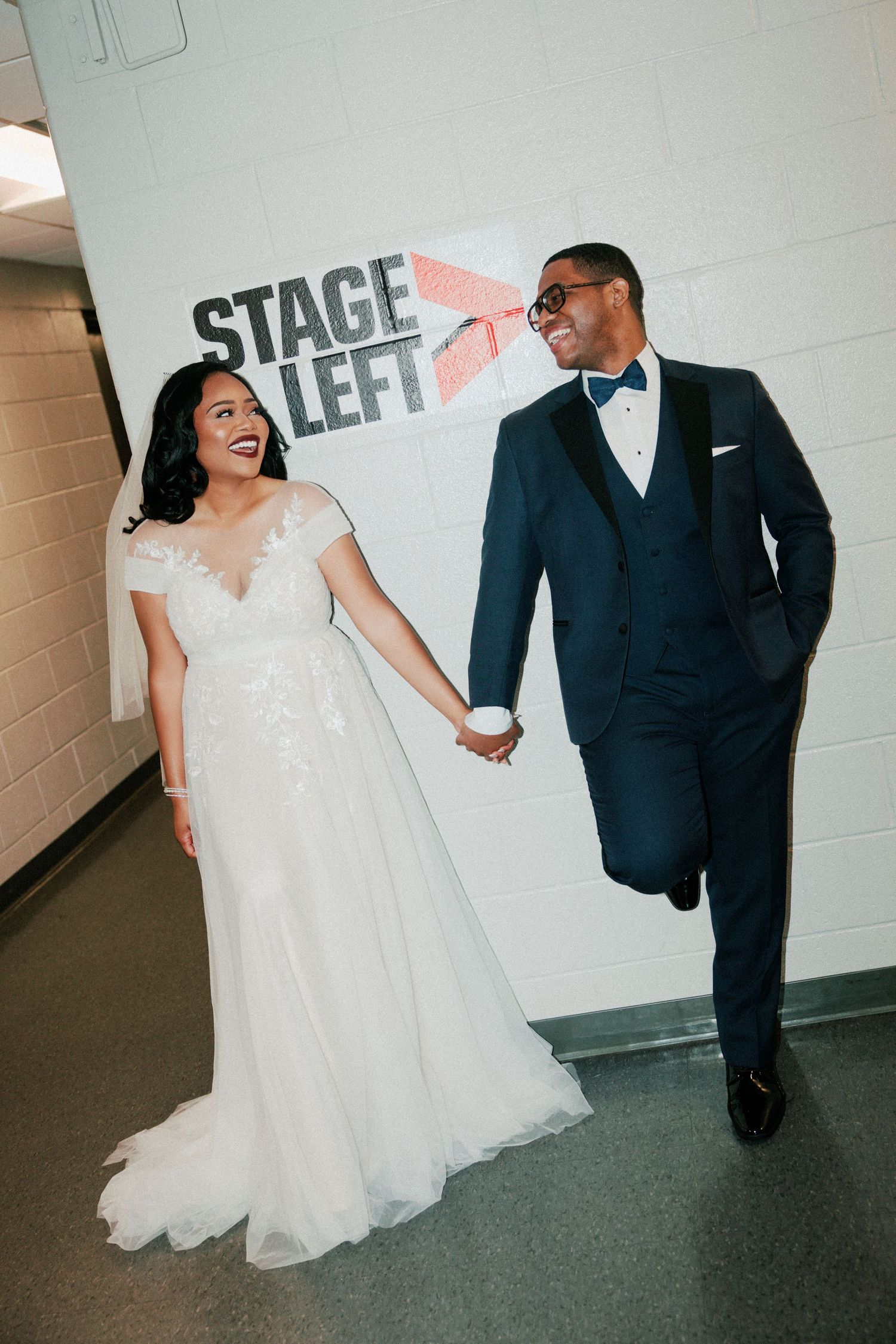 Happy couple walking hand in hand past a Stage Left sign in a hallway.