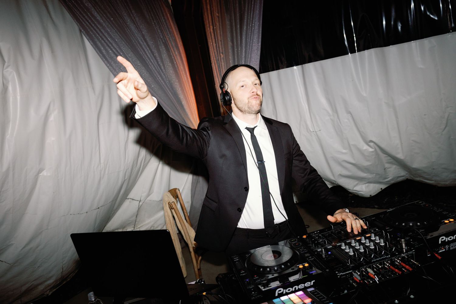 A DJ performs at a wedding reception with professional equipment under draped fabric decor.