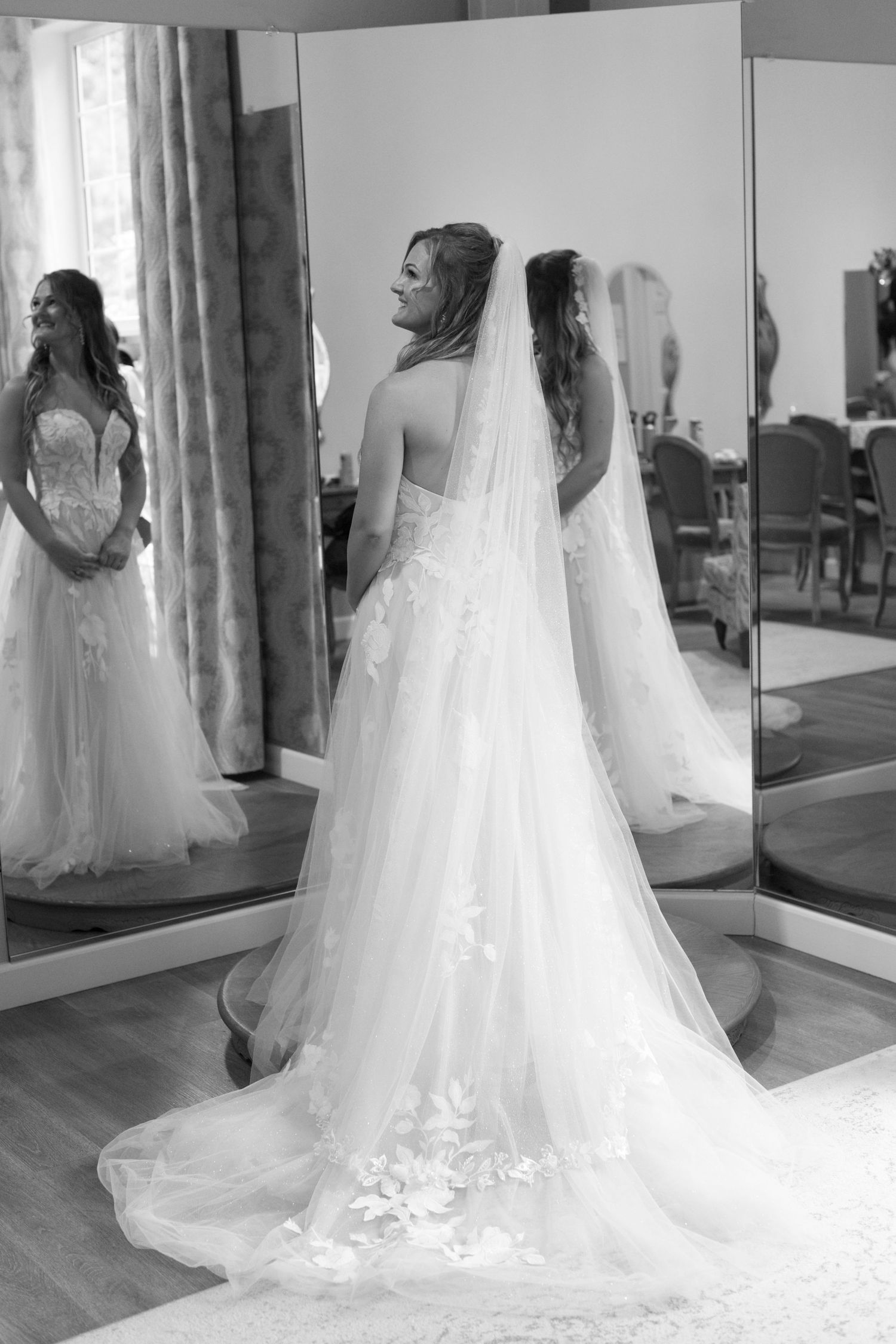 Multiple reflections of a wedding dress in full-length mirrors showing intricate train details.