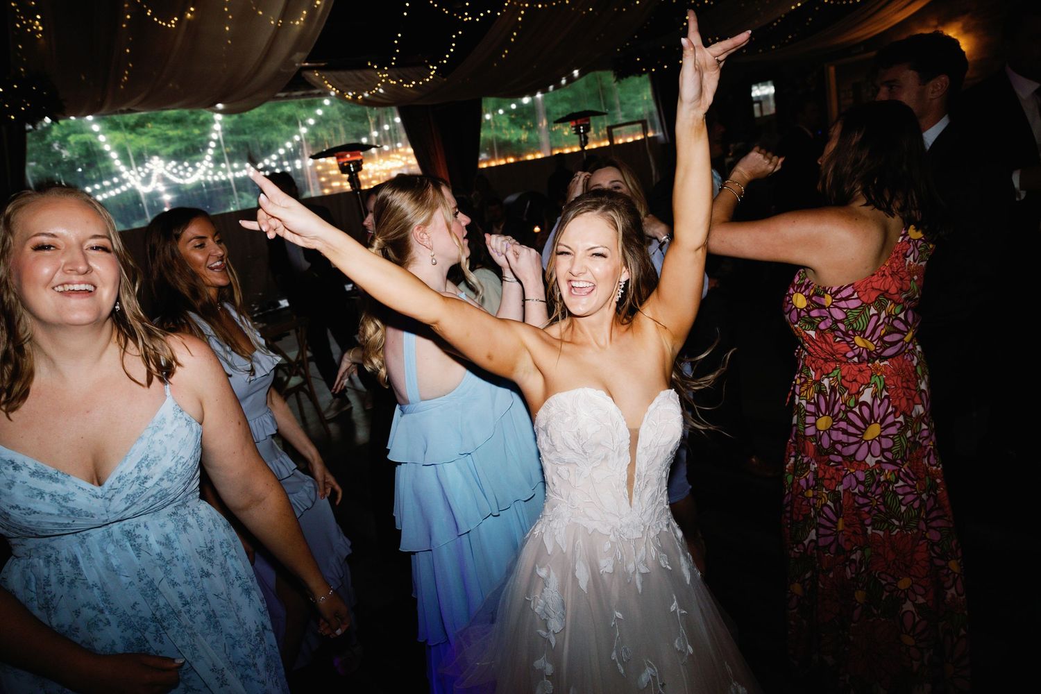 Wedding guests dance and celebrate on darkened reception dance floor with colorful attire.