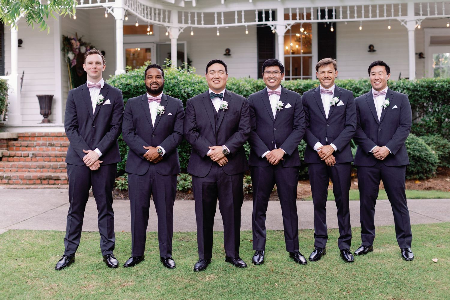 Wedding party members in formal attire pose together on a grand southern estate porch.