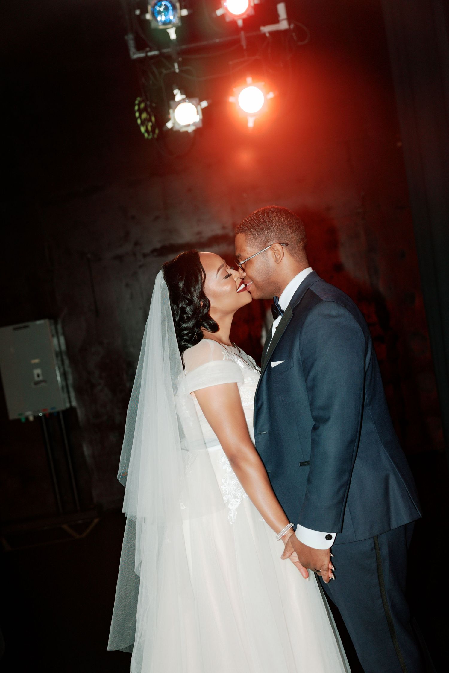Romantic wedding moment captured under dramatic red lighting and disco balls.