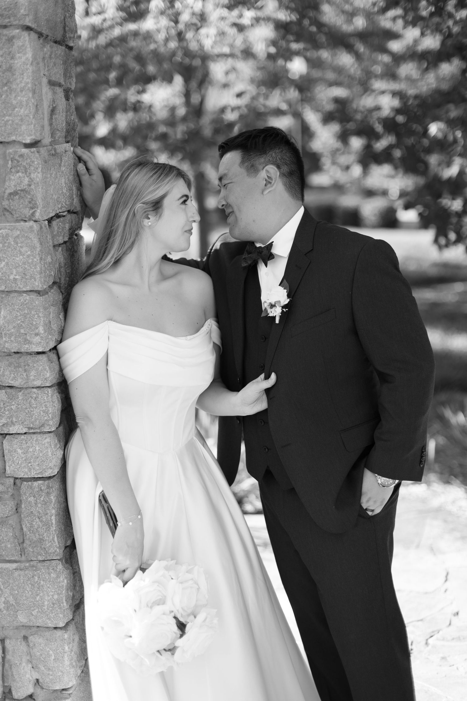 Black and white wedding portrait against stone wall with romantic pose.