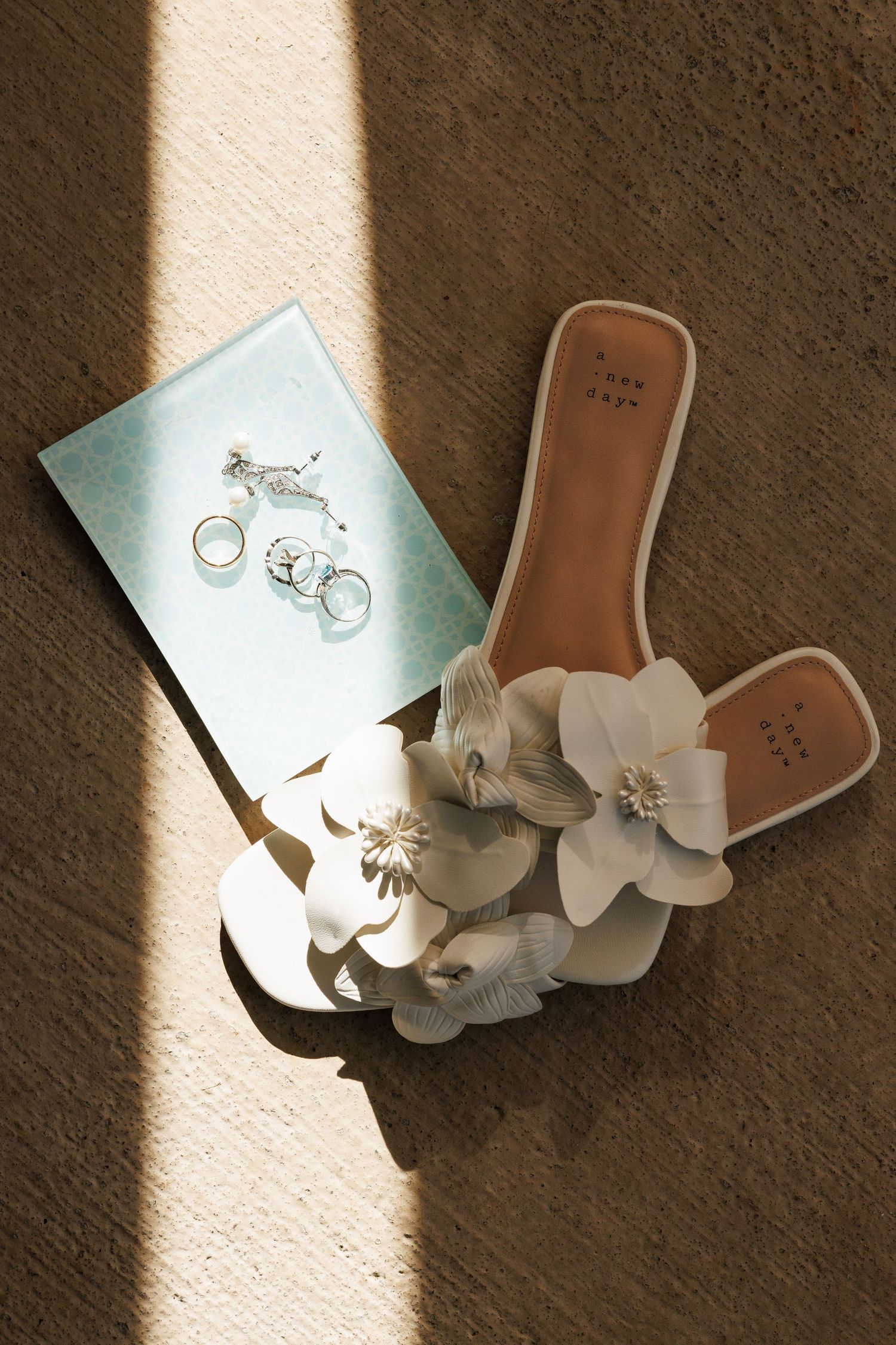 Wedding details including rings and floral decorations in natural sunlight.