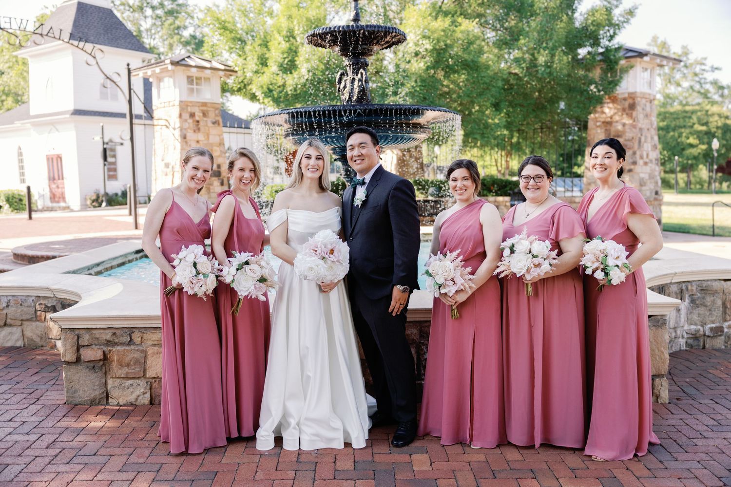 Wedding party in burgundy dresses and black suits poses together on brick patio.