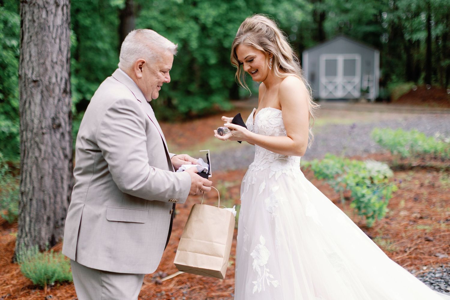 A sweet moment captured as two people exchange gifts on a stone pathway surrounded by pine trees.