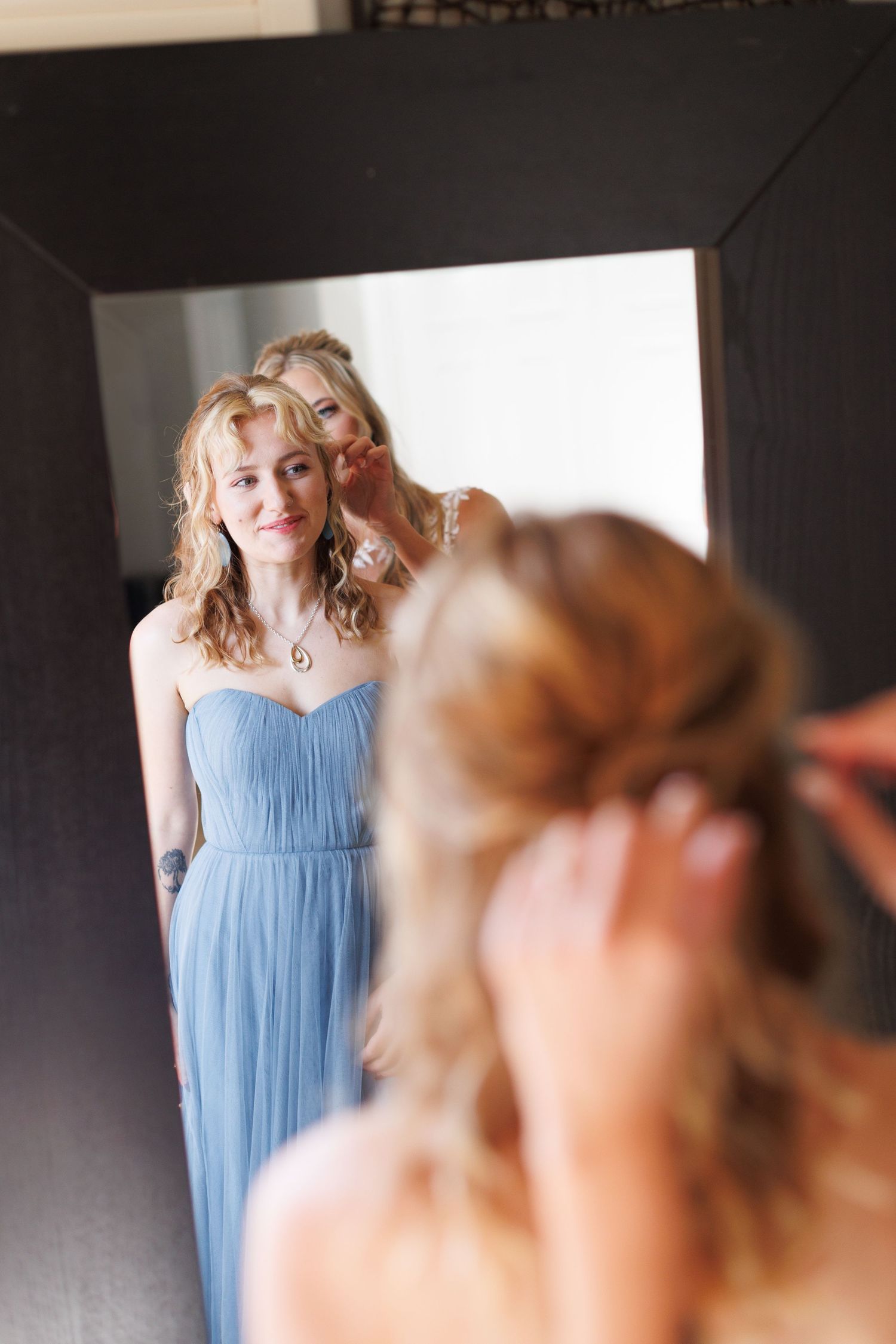 A bridesmaid in a flowing light blue dress smiles during wedding preparations.