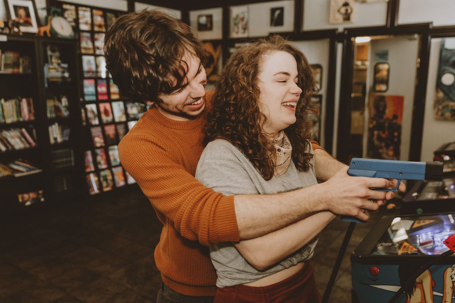 Playful couple laughing while playing arcade games together in a dimly lit gaming venue.