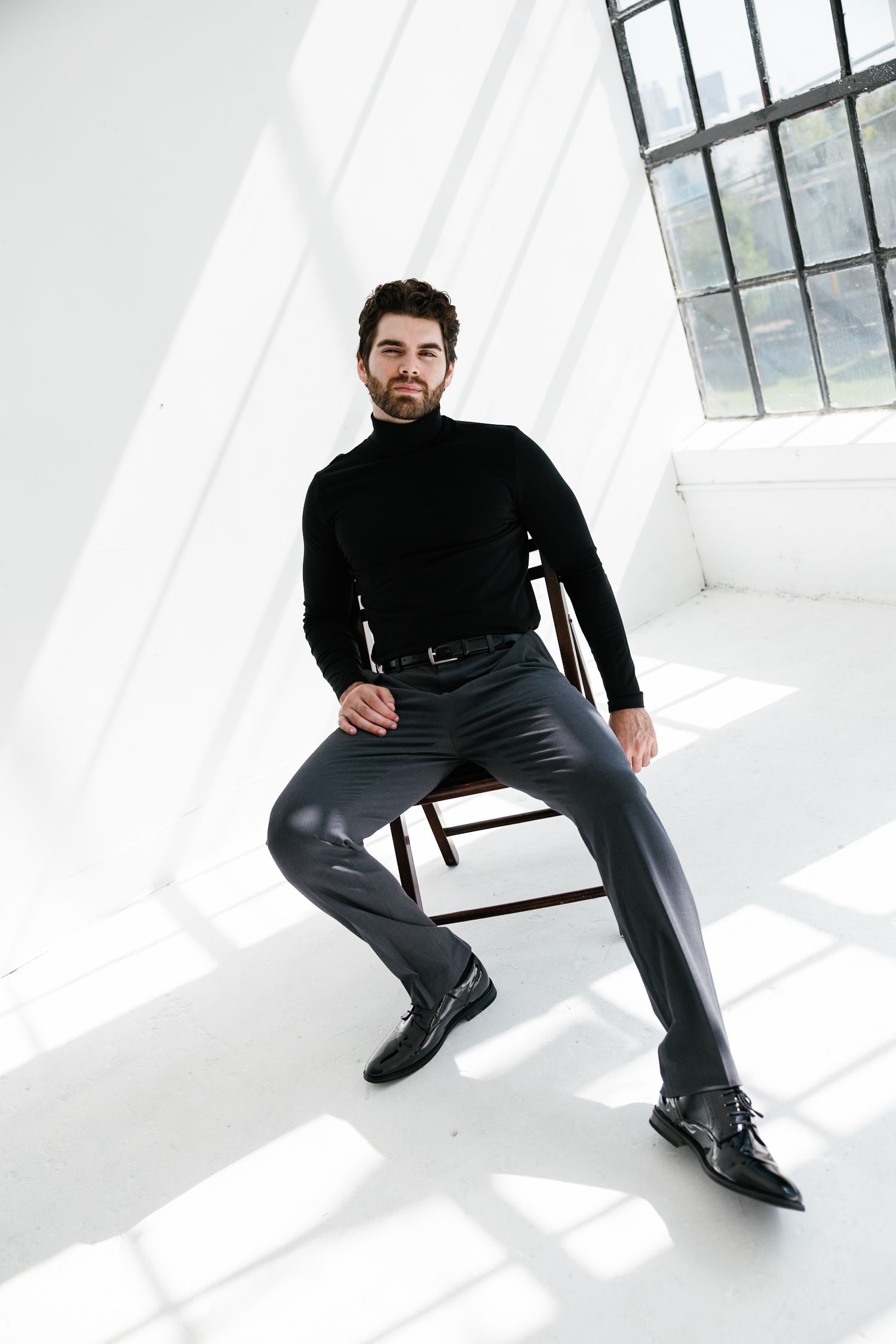 Model in all black outfit strikes dramatic poses in sunlit studio.