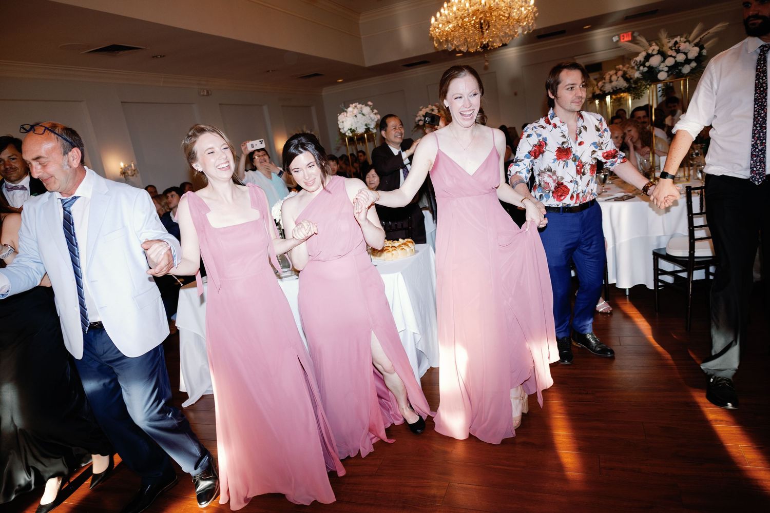 Wedding celebration with bridesmaids in pink dresses dancing on wooden floor.
