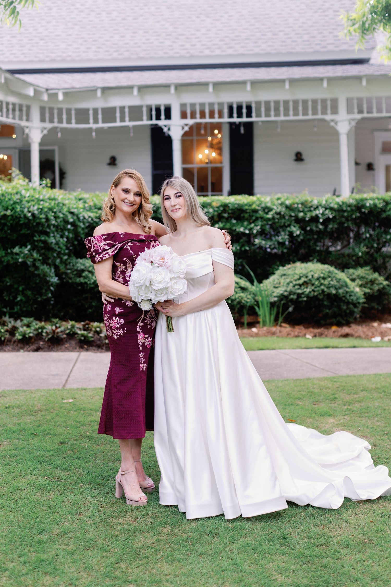 Bridal photos featuring burgundy and white gowns on a sunny lawn with white building backdrop.
