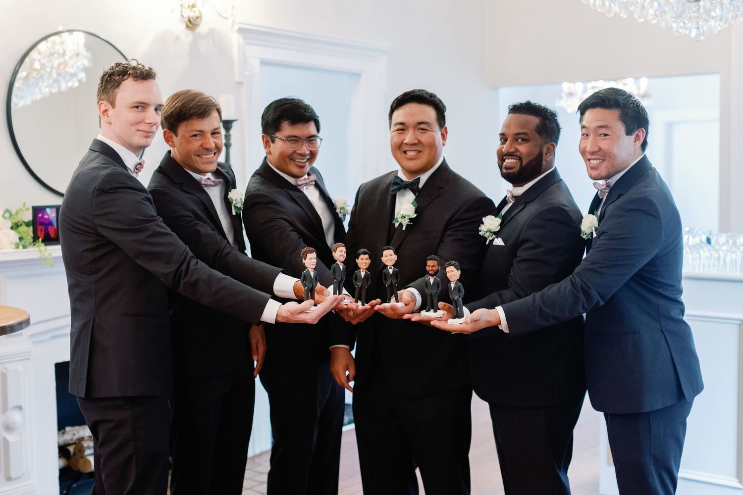 Groomsmen in black tuxedos gather for a playful photo shoot indoors.