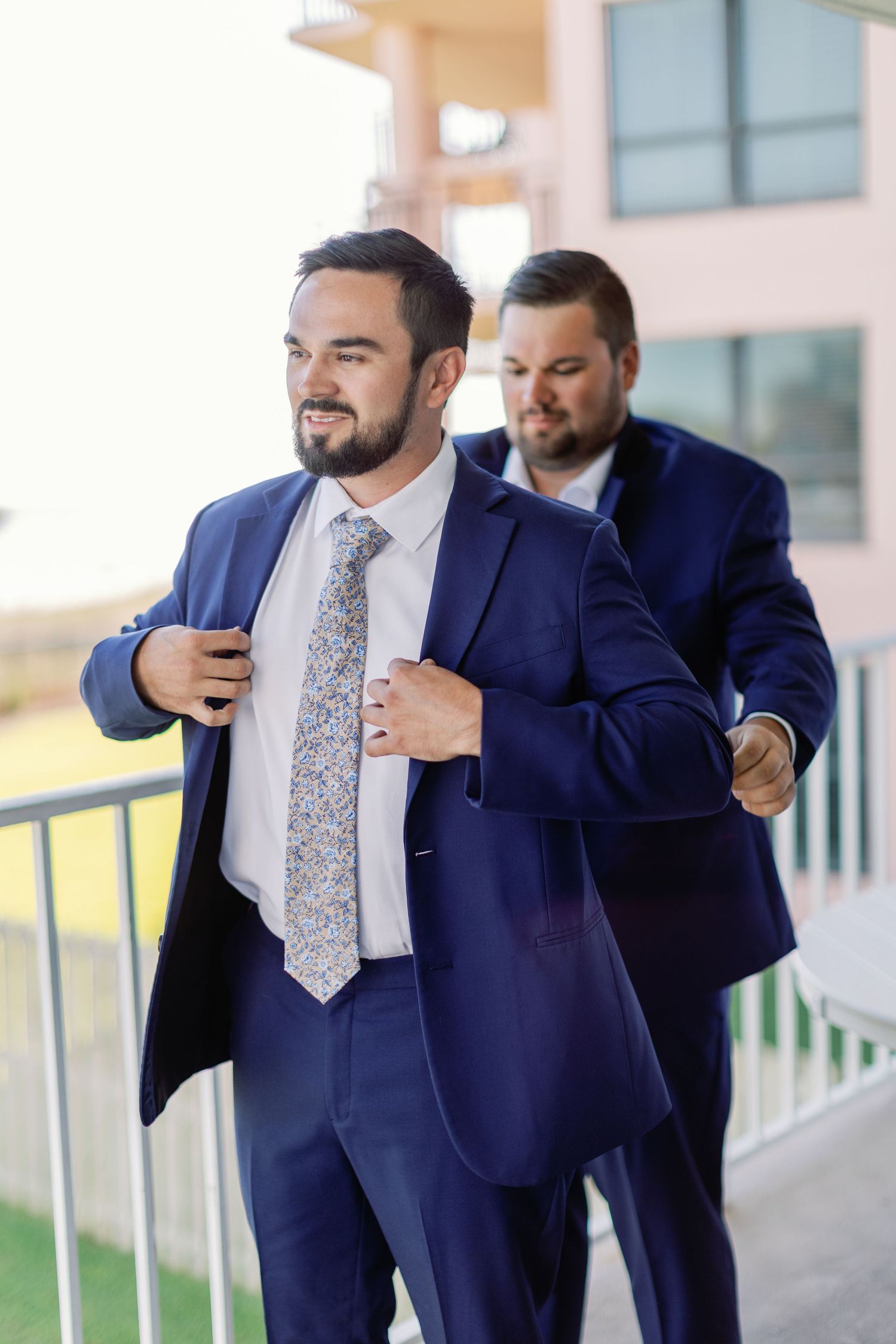 Multiple angles of a groom adjusting his tie while standing on an outdoor balcony.