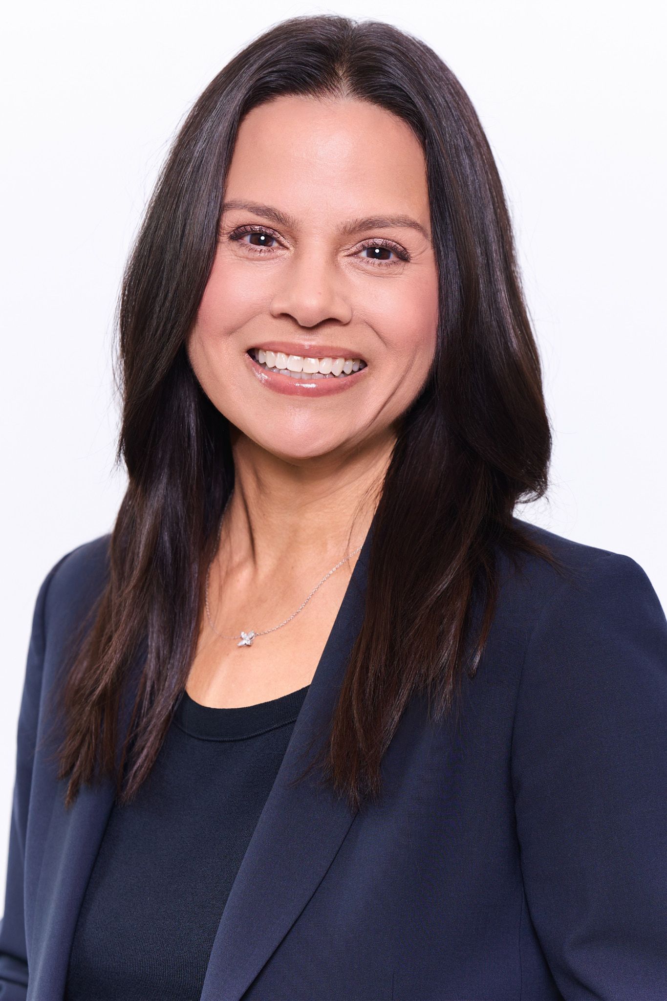 Professional headshot series of person in black top and navy blazer smiling against white background.