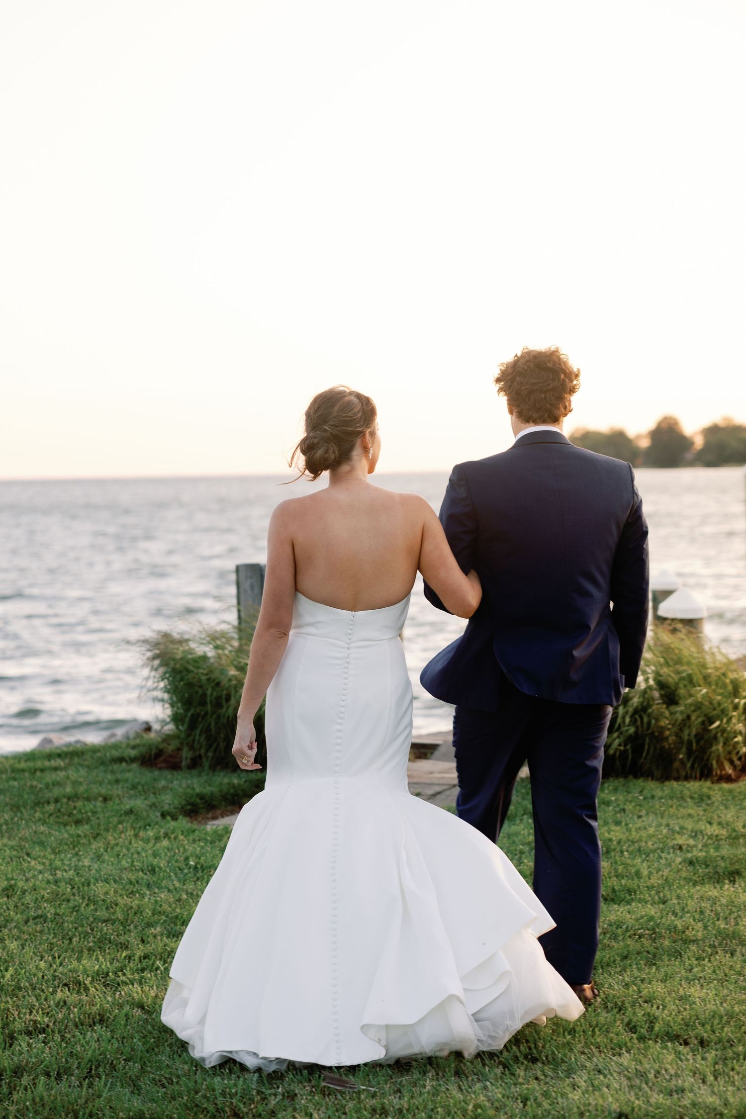 Bride and groom sit together watching sunset by the ocean during outdoor wedding photoshoot.
