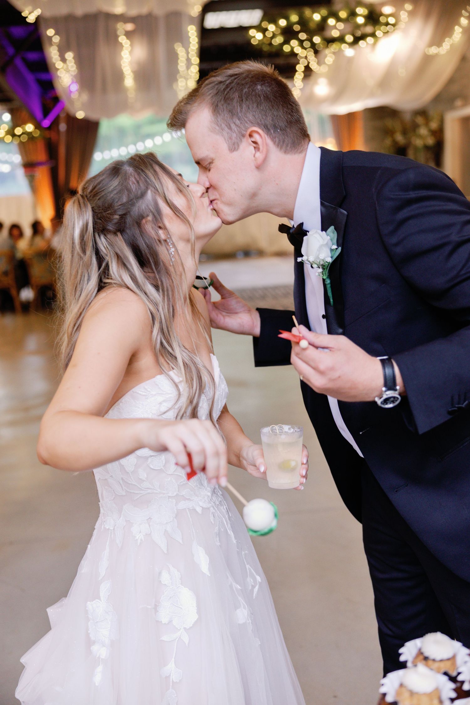 Newlyweds share dessert during reception with string lights twinkling in background.