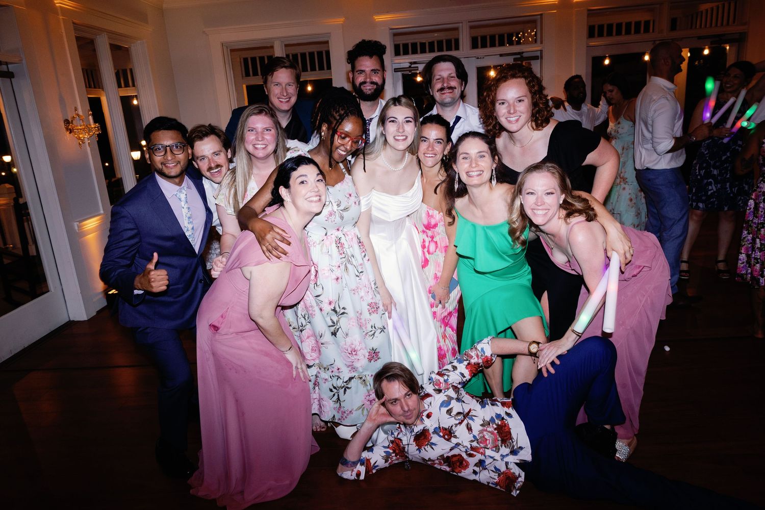 A group of wedding guests celebrates with glow sticks during an evening reception.
