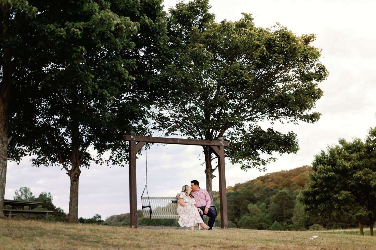Distant silhouettes of a couple standing together on a hilltop against a scenic landscape.