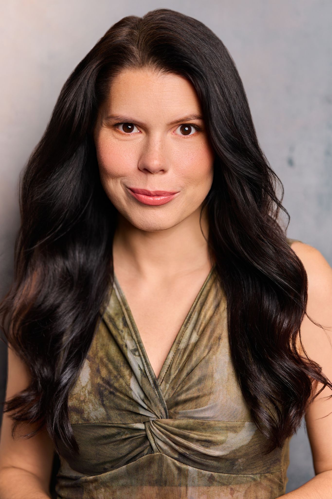 A woman with long dark hair wearing a green halter top poses for a professional headshot photo.