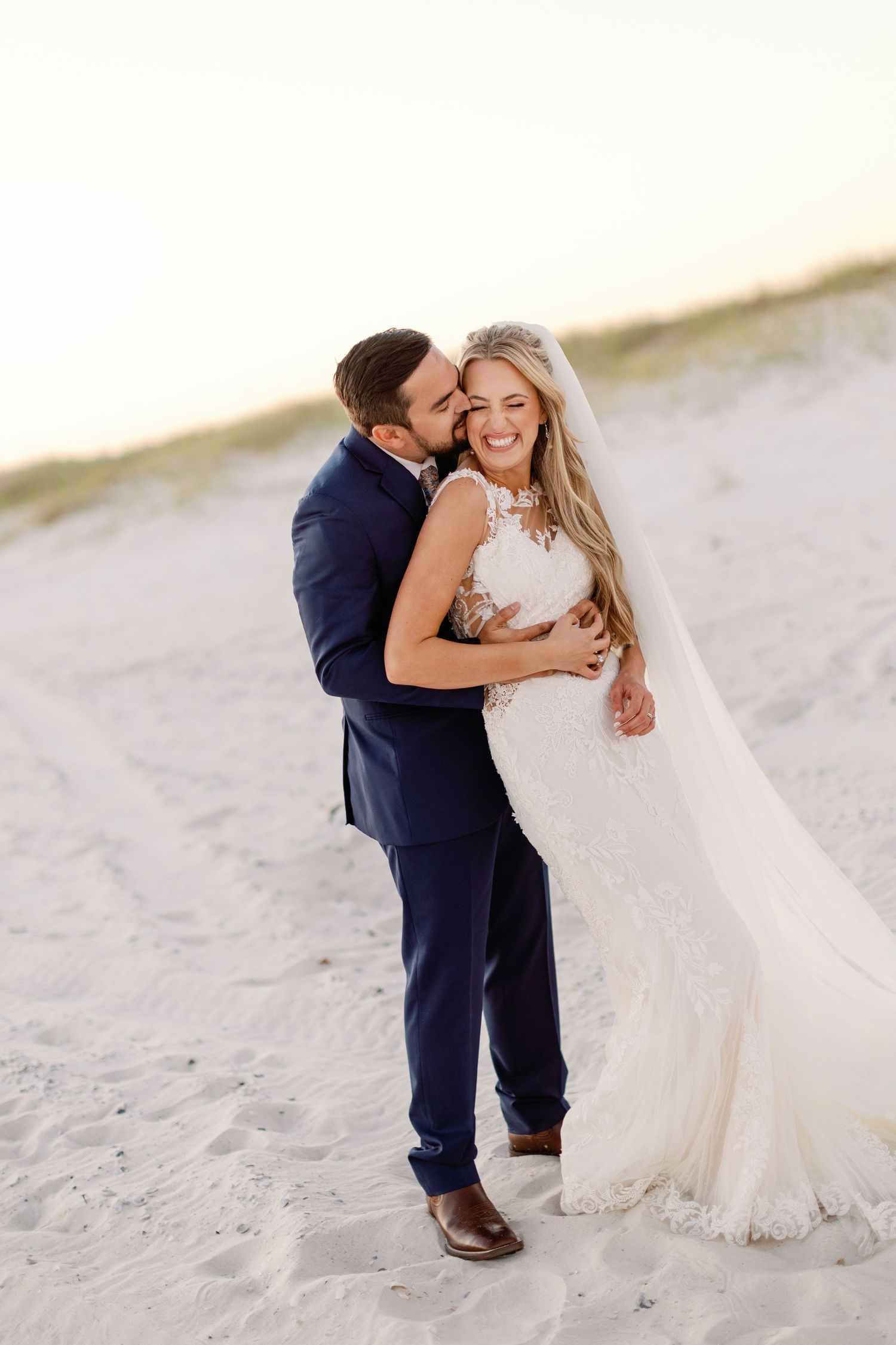 Newlywed couple shares playful moments on a white sandy beach in formalwear.