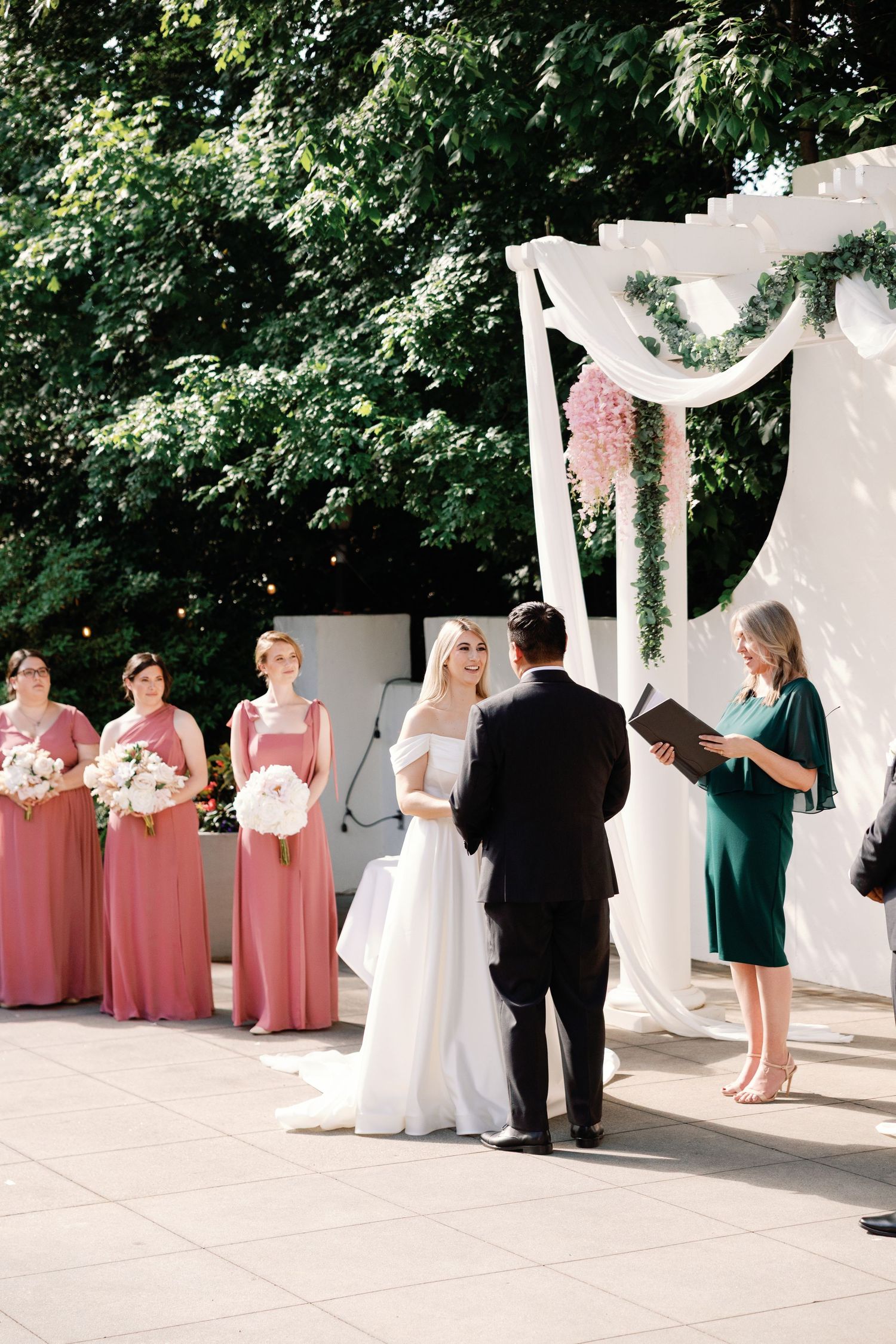 Wedding party in pink and green dresses poses during an outdoor ceremony.