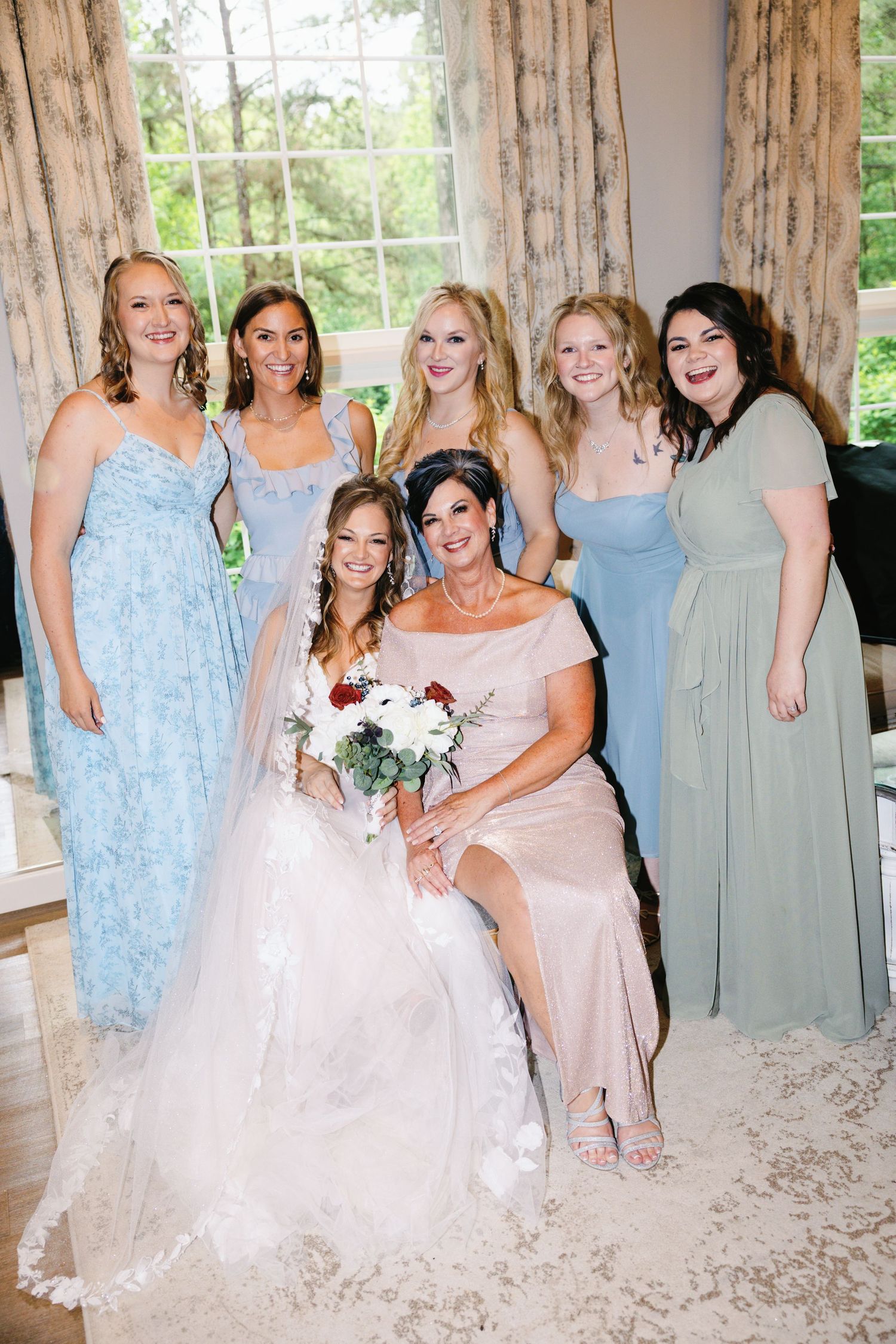 Wedding party wearing pastel blue and pink dresses pose together in natural light.