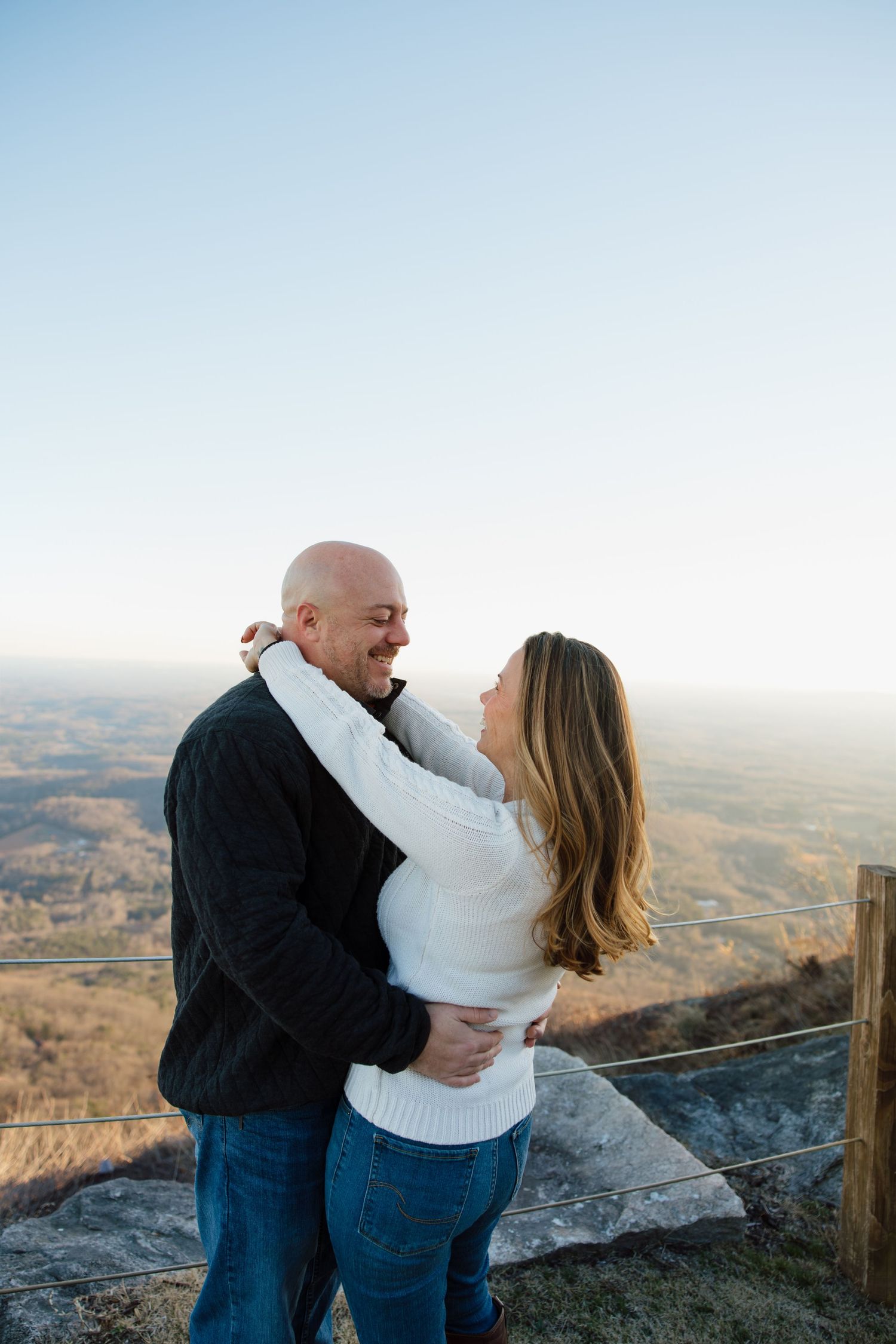 Couple sharing romantic embrace on mountain overlook during sunset.